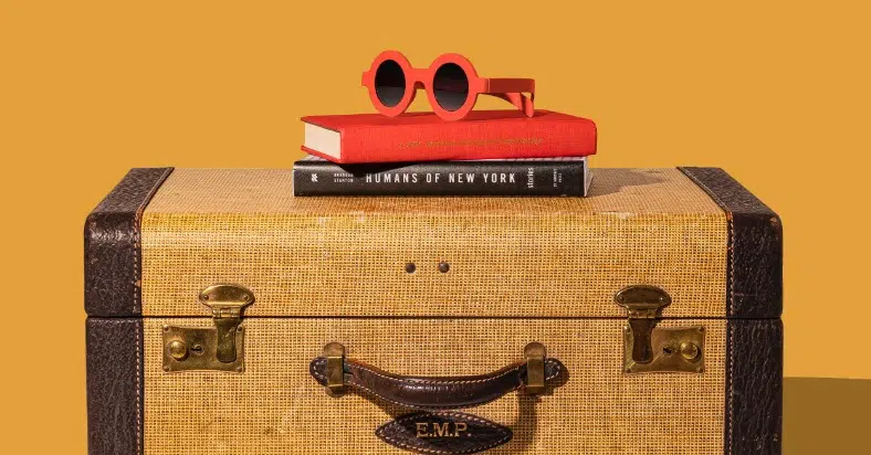 Two books and sunglasses on top of a suitcase