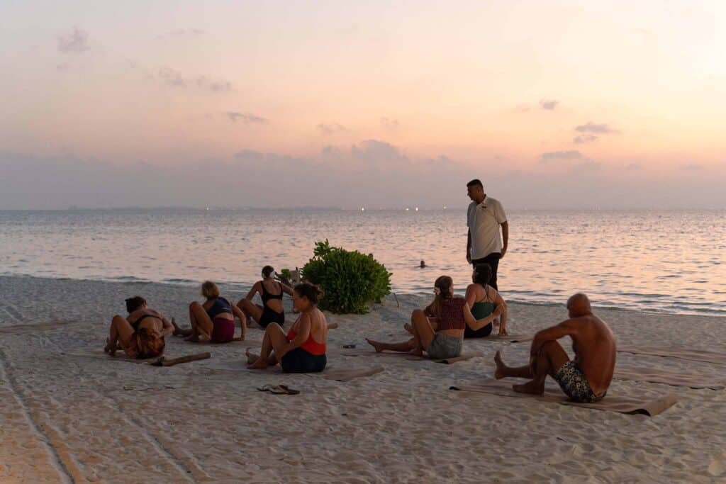 Peaceful evening yoga session on Dhoni Bar Beach at sunset at Canareef Resort Maldives.