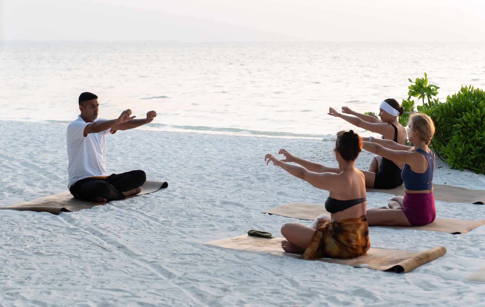 Yoga session at Dhoni Bar Beach with guests practicing yoga at sunset at Canareef Resort Maldives.
