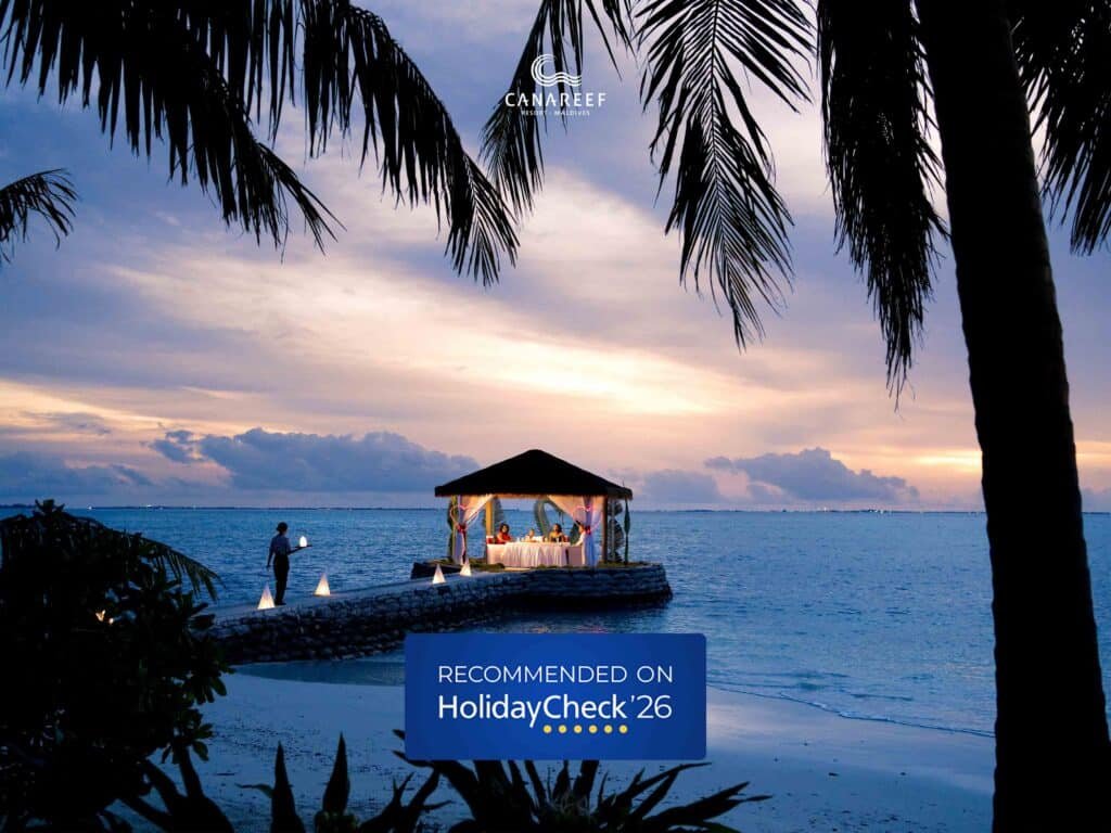 A romantic sunset dinner setup on a private jetty at Canareef Resort Maldives with the HolidayCheck 2026 Recommended Resort badge
