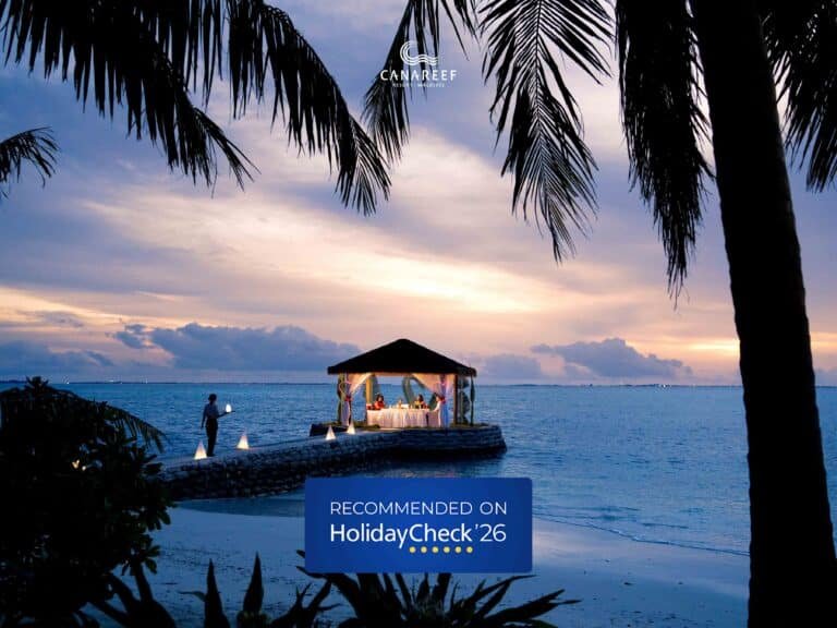 A romantic sunset dinner setup on a private jetty at Canareef Resort Maldives with the HolidayCheck 2026 Recommended Resort badge